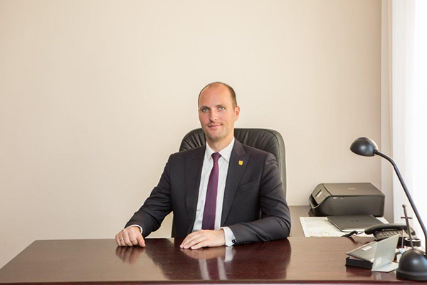 Fotografia przedstawia burmistrza Konrada Malickiego. Mężczyzna w garniturze siedzi za biurkiem, pozując. Zdjęcie pochodzi z archiwum prywatnego.